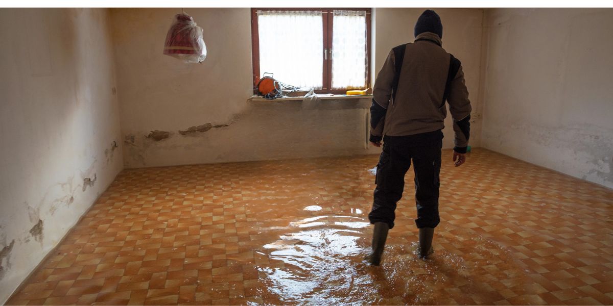 Flooded basement with standing water and severe water damage—man assessing need for basement waterproofing
